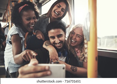 Diverse group of young friends smiling and taking a selfie together while riding on a bus - Powered by Shutterstock