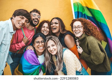Diverse group of young people celebrating gay pride festival day - Lgbt community concept with guys and girls hugging together outdoors - Multiracial trendy friends standing on a yellow background 
