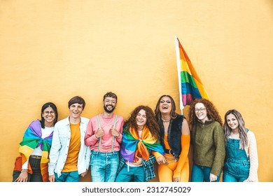 Diverse group of young people celebrating gay pride festival day - Lgbt community concept with guys and girls hugging together outdoors - Multiracial cheerful friends standing on a yellow background 