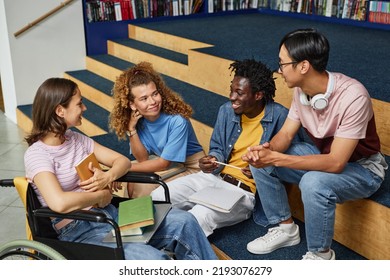 Diverse Group Of Young People Discussing Work In College Library Including Female Student With Disability