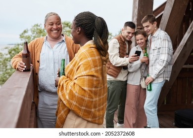 Diverse Group Young People Drinking Beer On Balcony During Party At Lake House