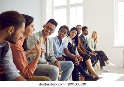 Diverse group of young people sitting in row in modern office and talking. Happy multi-racial men and women having interesting discussion during business meeting or psychological training - Powered by Shutterstock