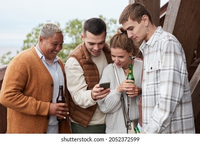 Diverse Group Young People Using Smartphone On Balcony During Party At Lake House