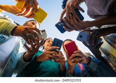 Diverse group of young people using mobile phone device standing together in circle outdoors. Millennial friends addicted to social media app, betting or playing video game on platform online. - Powered by Shutterstock