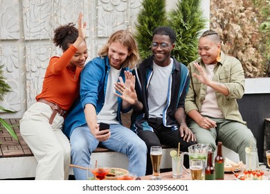 Diverse Group Of Young People Waving At Camera Via Video Chat While Having Fun During Outdoor Party At Rooftop