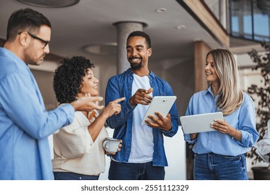 A diverse group of young professionals enjoy a collaborative discussion, using digital tablets in a modern, open office space. They are engaged, smiling, and creatively exchanging ideas.