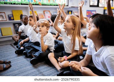 Diverse group of young students, boys and girls, sit on the floor in a classroom raising hands. Diverse students raise their hands, engaged in a classroom activity. Students raise hand in classroom. - Powered by Shutterstock