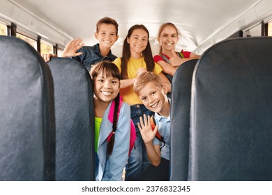 Diverse happy cheerful kids having fun inside a school bus, waving enthusiastically at the camera, smiling pupils posing together, sharing joyful moments during their ride to school - Powered by Shutterstock