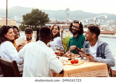 Diverse happy friends having dinner party outside sitting around table at rooftop terrace. Millennial people enjoying a meal during sunset, celebrating together. - Powered by Shutterstock