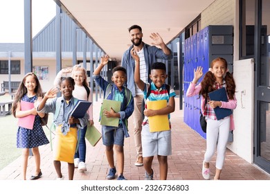 Diverse, happy male teacher and elementary schoolchildren waving in school corridor, copy space. Education, inclusivity, elementary school and learning concept. - Powered by Shutterstock