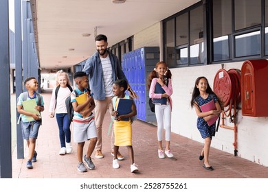 Diverse, happy male teacher and elementary schoolchildren walking in school corridor, copy space. Education, inclusivity, elementary school and learning concept. - Powered by Shutterstock