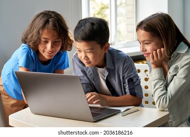 Diverse happy school kids using laptop computer together in classroom. Multicultural children junior students classmates learning online elementary education program class gathered at desk. - Shutterstock ID 2036186216
