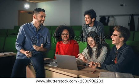 Diverse Happy Students Having a Conversation with a Teacher in University Classroom, Working on a Shared Research Project on a Laptop Computer. Classmates Working Together on College Science Project