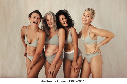 Diverse And Happy Women Posing In Their Natural Bodies. Four Confident Women Of Different Ages Wearing Underwear And Smiling Cheerfully. Women Embracing Each Other Against A Studio Background.