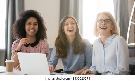 Diverse Happy Young And Old Businesswomen Laughing Looking Away Engaged In Shared Corporate Meeting, Joyful Multi-ethnic Women Different Age Generation Employees Sit With Laptop Having Fun At Work