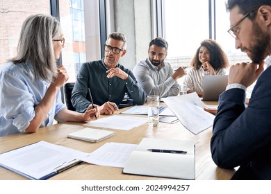 Diverse international executive business partners group discuss report at boardroom meeting table. Multiracial team negotiating project developing business strategy doing paperwork analysis in office. - Powered by Shutterstock