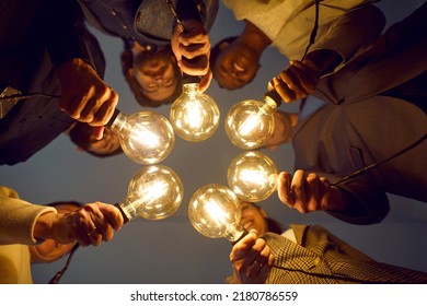 Diverse Interracial Team Of Smiling Business Professionals Holding Bright Electric Edison Light Bulbs As Symbol Of Sharing Creative Modern Startup Project Ideas. View From Below. Conceptual Background