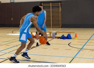 Diverse male basketball players wearing blue sports clothes and playing basketball at gym. Sport, activity, togetherness and lifestyle, unaltered, copy space. - Powered by Shutterstock