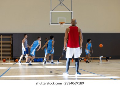 Diverse male basketball players wearing blue sports clothes and playing basketball with coach at gym. Sport, activity, teamwork and lifestyle, unaltered, copy space. - Powered by Shutterstock