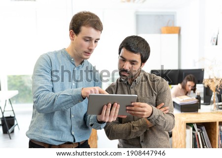 Diverse male coworkers chating and giving their opinion while looking a tablet at the office.