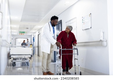 Diverse male doctor helping senior female patient use walking frame in hospital corridor, copy space. Hospital, medical and healthcare services. - Powered by Shutterstock