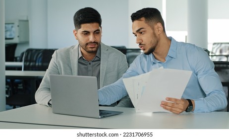 Diverse male employees Arab young colleagues discussing working together, checking emails. Two serious focused East Indian businessmen sitting in modern office using laptop looking at computer screen - Shutterstock ID 2231706955