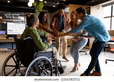 Diverse male and female colleagues stacking hands at casual office meeting. Casual office, teamwork, disability, inclusivity, business and work, unaltered. - Powered by Shutterstock