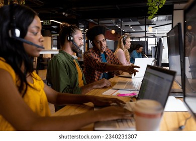 Diverse male and female creative colleagues working using phones headsets and computers in office. Casual office, teamwork, communication, business and work, unaltered. - Powered by Shutterstock