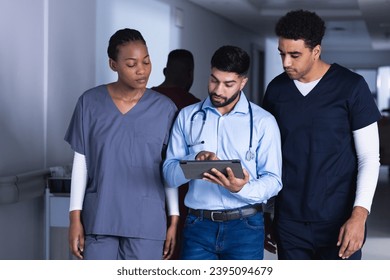 Diverse male and female doctors using tablet walking in hospital corridor. Medicine, healthcare, communication and medical services, unaltered. - Powered by Shutterstock