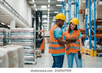 A diverse male and female employee in safety gear review inventory data using a clipboard and scanner, exemplifying teamwork, precision, and the intersection of workforce and technology. - Powered by Shutterstock