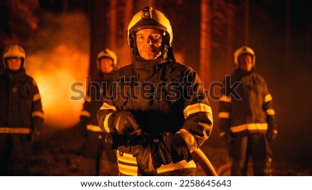 Diverse Male and Female Team of Professional Firefighters Standing in a Smoked Out Forest During a Wildland Fire, Posing and Looking at Camera. Group Wearing Protective Clothing, Helmets and Gear.