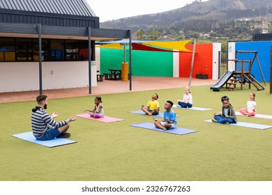 Diverse male teacher and elementary schoolchildren practicing meditation in schoolyard. Education, inclusivity, elementary school and learning concept. - Powered by Shutterstock