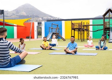 Diverse male teacher and elementary schoolchildren practicing meditation in schoolyard. Education, inclusivity, elementary school and learning concept. - Powered by Shutterstock