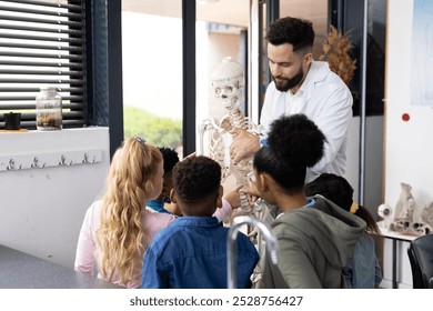 Diverse male teacher and elementary schoolchildren studying skeleton in biology class. Education, inclusivity, elementary school and learning concept. - Powered by Shutterstock