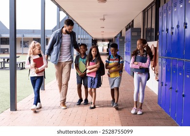 Diverse male teacher and happy elementary schoolchildren walking in school corridor, copy space. Education, inclusivity, elementary school and learning concept. - Powered by Shutterstock