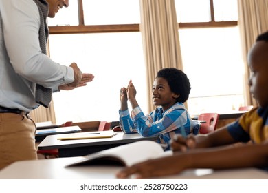 Diverse male teacher teaching school boy using sign language in class at elementary school. School, disability and education, unaltered. - Powered by Shutterstock