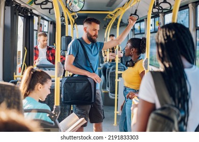 Diverse man and woman couple passengers talking while riding in a bus. Young diverse people going to work by public transport. African American woman talking to her male friend while traveling by bus.