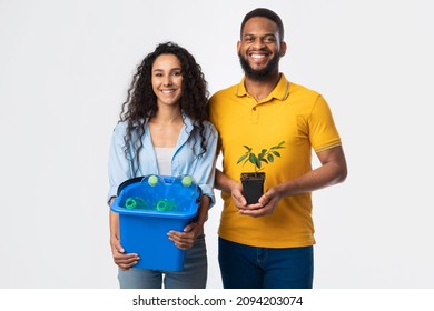 Diverse Man And Woman Holding Green Plant And Plastic Bottles In Garbage Bucket Posing Smiling To Camera Standing On White Studio Background. Keep Environment Clean, Care For Nature Concept