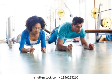 Diverse man and woman working out together and standing in plank position training abdomen together in gym - Powered by Shutterstock