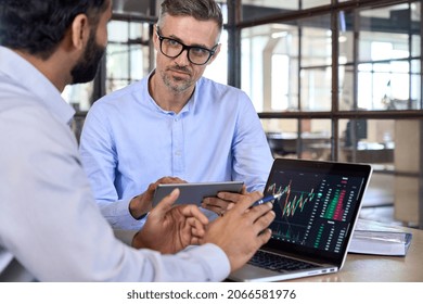 Diverse managers traders analysts discussing financial growth market at desk with laptop with graphs on screen using tablet device. Investors brokers analysing indexes online cryptocurrency stock.