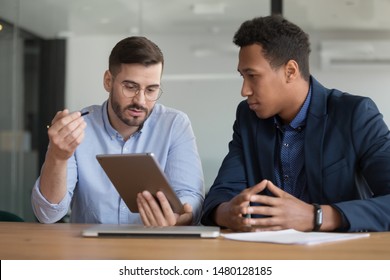 Diverse mates working on startup project use tablet discuss online apps, caucasian company representative meet with client showing explain offering presenting new services on electronic gadget concept