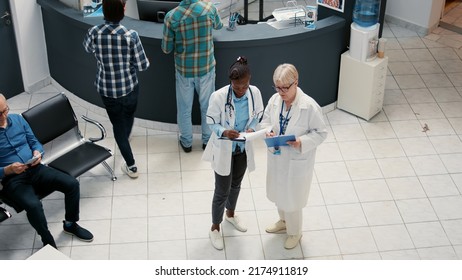 Diverse Medical Team Of Doctors Talking And Writing Report In Hospital Reception Area, Working In Healthcare System To Support Sick Patients. Appointments In Waiting Room Lobby.