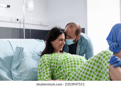 Diverse medical team helping woman with pregnancy to delivery baby in hospital ward. Pregnant patient having painful contractions being comforting by husband while giving birth to child - Powered by Shutterstock