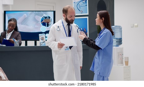 Diverse Medical Team Talking About Healthcare Support In Reception Lobby At Healthcare Clinic. Analyzing Report Papers To Help With Recovery Treatment In Waiting Room Area, Checkup Visit.