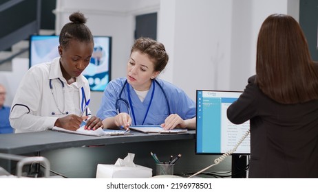 Diverse Medical Team Working At Hospital Reception Desk Ith Receptionist, Analyzing Checkup Papers To Help With Healthcare Appointments. Specialists Writing Insurance Report At Registration Counter.