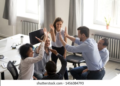 Diverse Millennial Colleagues Give High Five Engaged In Informal Teambuilding Activity In Office, Multiracial Young Coworkers Involved In Creative Group Meeting, Have Motivational Briefing Or Talk