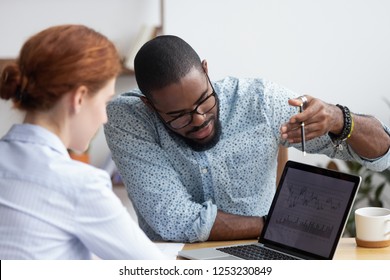 Diverse Millennial Colleagues Working Together Analyzing Diagram Looking At Computer Screen. Black Mentor Helps Female Apprentice Understand Corporate Program Explaining Interface Showing On Monitor