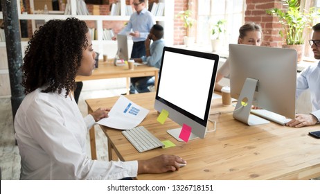 Diverse Millennial Employees Working In Modern Cozy Coworking Space Focus On Black African Worker Sitting At Desk Using Computer Typing Business Message Looking At Device Screen Holding Paper Document