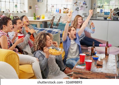 Diverse mix of friends sports fans watching winning football match on TV at home Celebrating winning goal huddled on couch shouting excited  sharing snacks drinking beer - Powered by Shutterstock