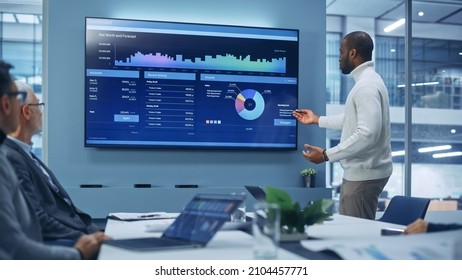 Diverse Modern Office: Motivated Black Businessman Leads Business Meeting With Managers, Talks, Uses Presentation TV With Statistics, Charts, Big Data. Digital Entrepreneurs Work On E-Commerce Project